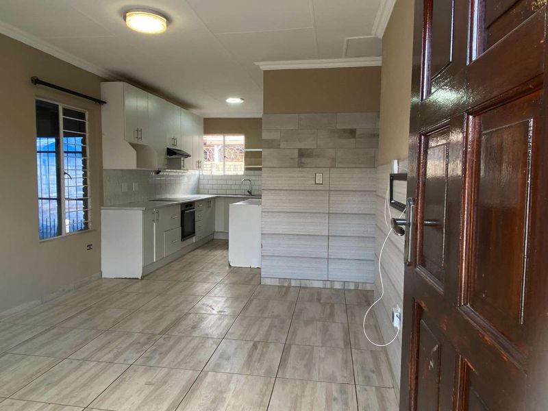 Open-plan living and kitchen area featuring modern tiled flooring, built-in cabinetry, integrated oven, and a decorative tiled feature wall.