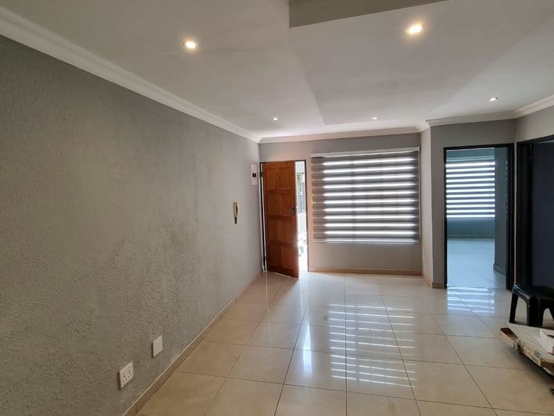 An empty living room featuring tiled flooring, recessed ceiling lighting, and modern roller blinds, offering a clean and neutral space ready for furnishing.