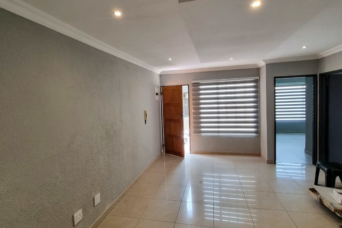 An empty living room featuring tiled flooring, recessed ceiling lighting, and modern roller blinds, offering a clean and neutral space ready for furnishing.