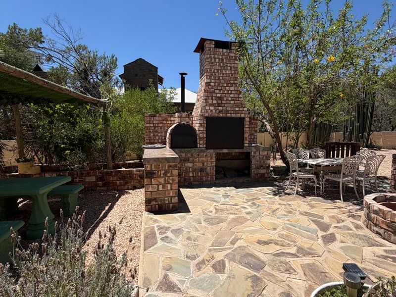 Outdoor patio area featuring a substantial brick built-in braai and pizza oven, complemented by stone paving and established garden surroundings.