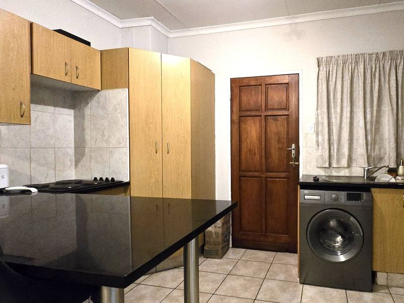 Functional kitchen featuring light wood cabinetry, black granite countertops, tiled backsplash, and integrated laundry facilities with tiled flooring.