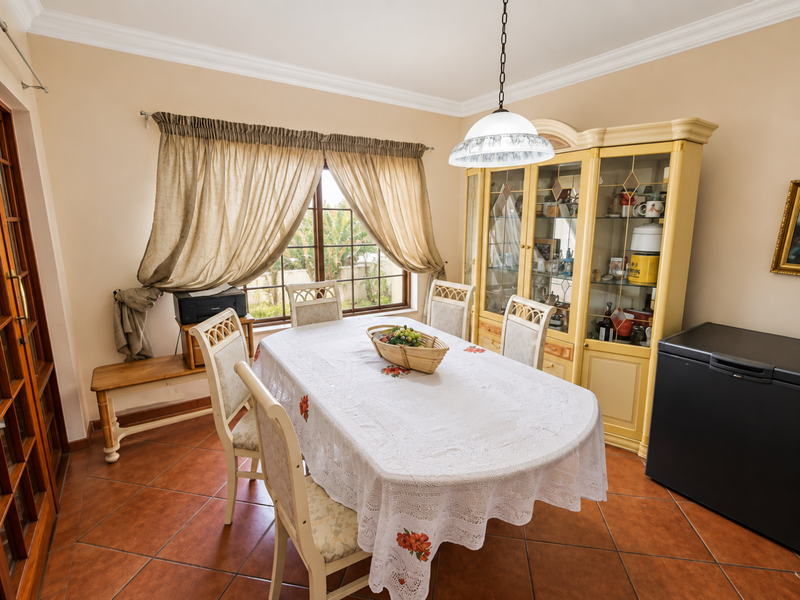 A dining room featuring terracotta floor tiles, crown molding, and a central pendant light fixture, with a window providing natural light.