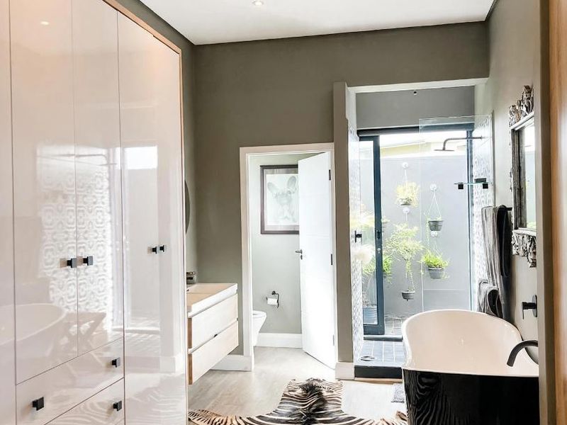 Modern bathroom featuring a sleek freestanding bathtub, extensive built-in cabinetry, a vanity, and a private walk-in shower area with access to a small courtyard.