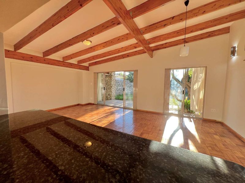 Spacious open-plan living area featuring exposed timber ceiling beams, parquet flooring, and dual sliding glass doors providing access to the outdoor space.