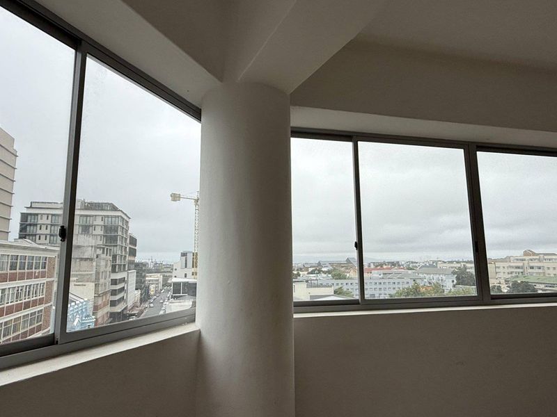 An empty office space featuring large aluminium-framed windows that provide extensive natural light and panoramic urban views.