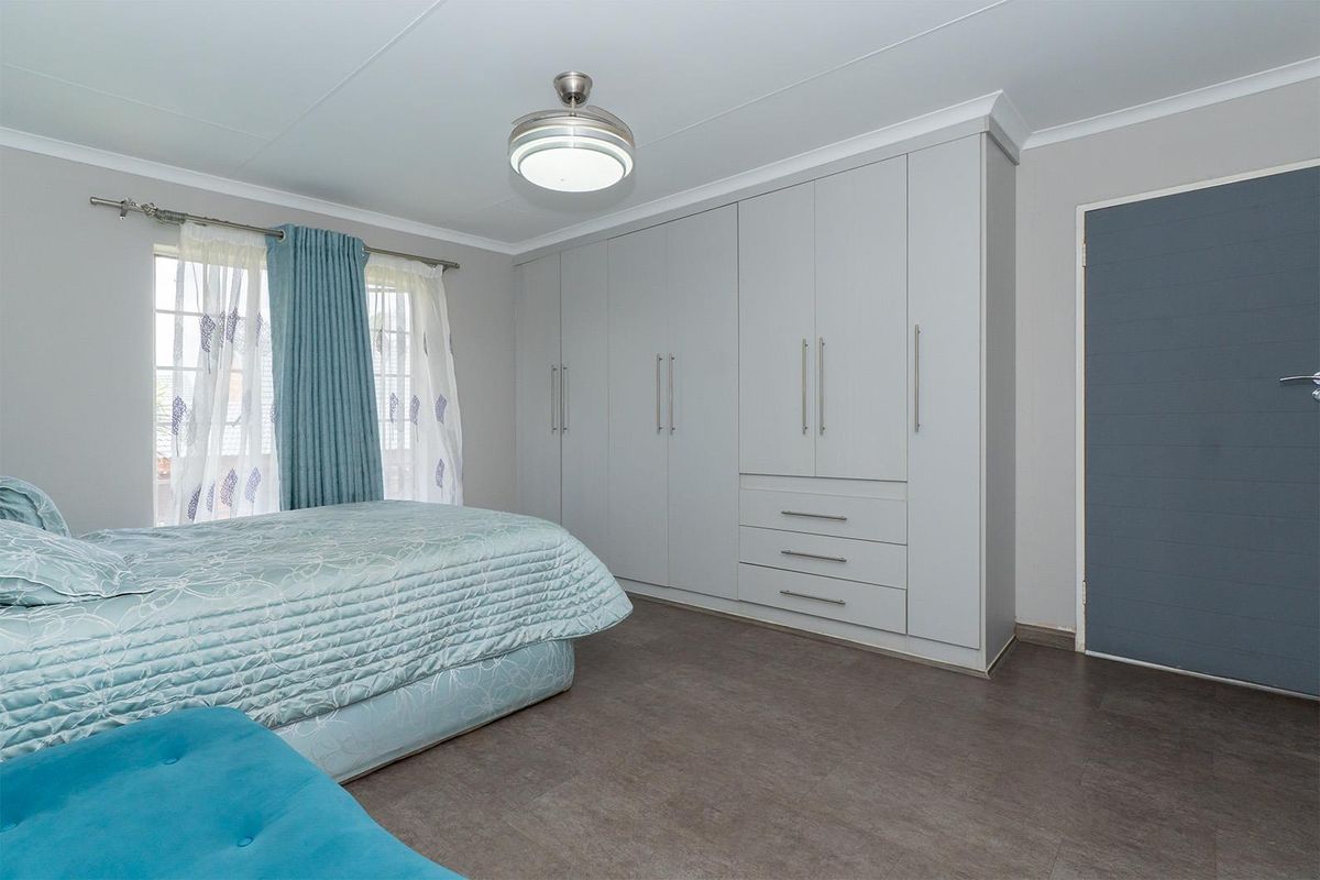 A well-maintained bedroom featuring extensive built-in cabinetry with integrated drawers and a modern ceiling fan light fixture.