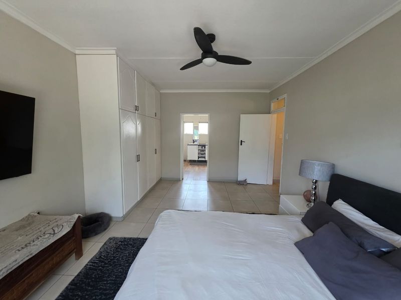 Spacious bedroom featuring built-in cupboards, tiled flooring, and a ceiling fan, with direct access to an adjoining room.