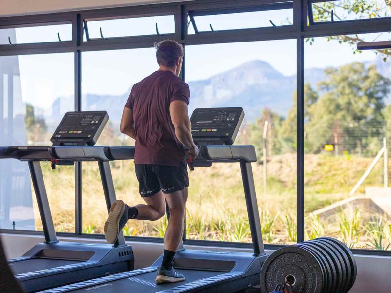 A modern gym facility featuring large glass windows with scenic mountain views and black aluminium frames.