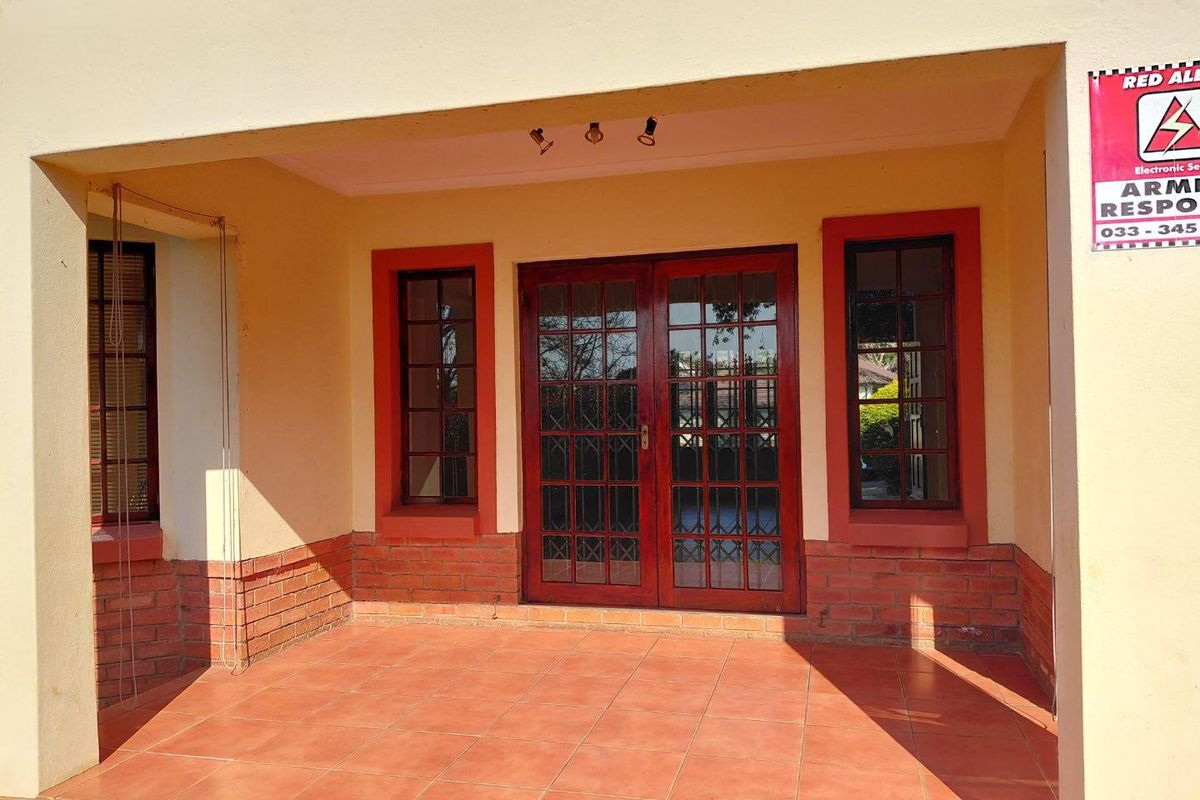A covered entrance porch featuring tiled flooring, a brick base, and double wooden doors with glass panes.