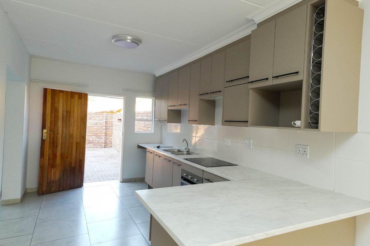 Modern kitchen featuring sleek cabinetry, marble-look countertops, integrated hob and oven, and direct access to an outdoor paved area.