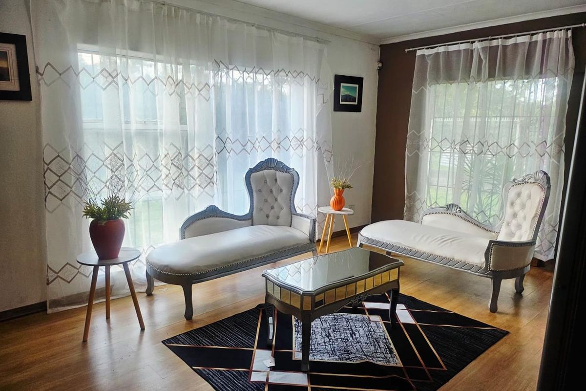 A bright living room featuring wood-look flooring, large windows with sheer curtains, and a neutral color palette.