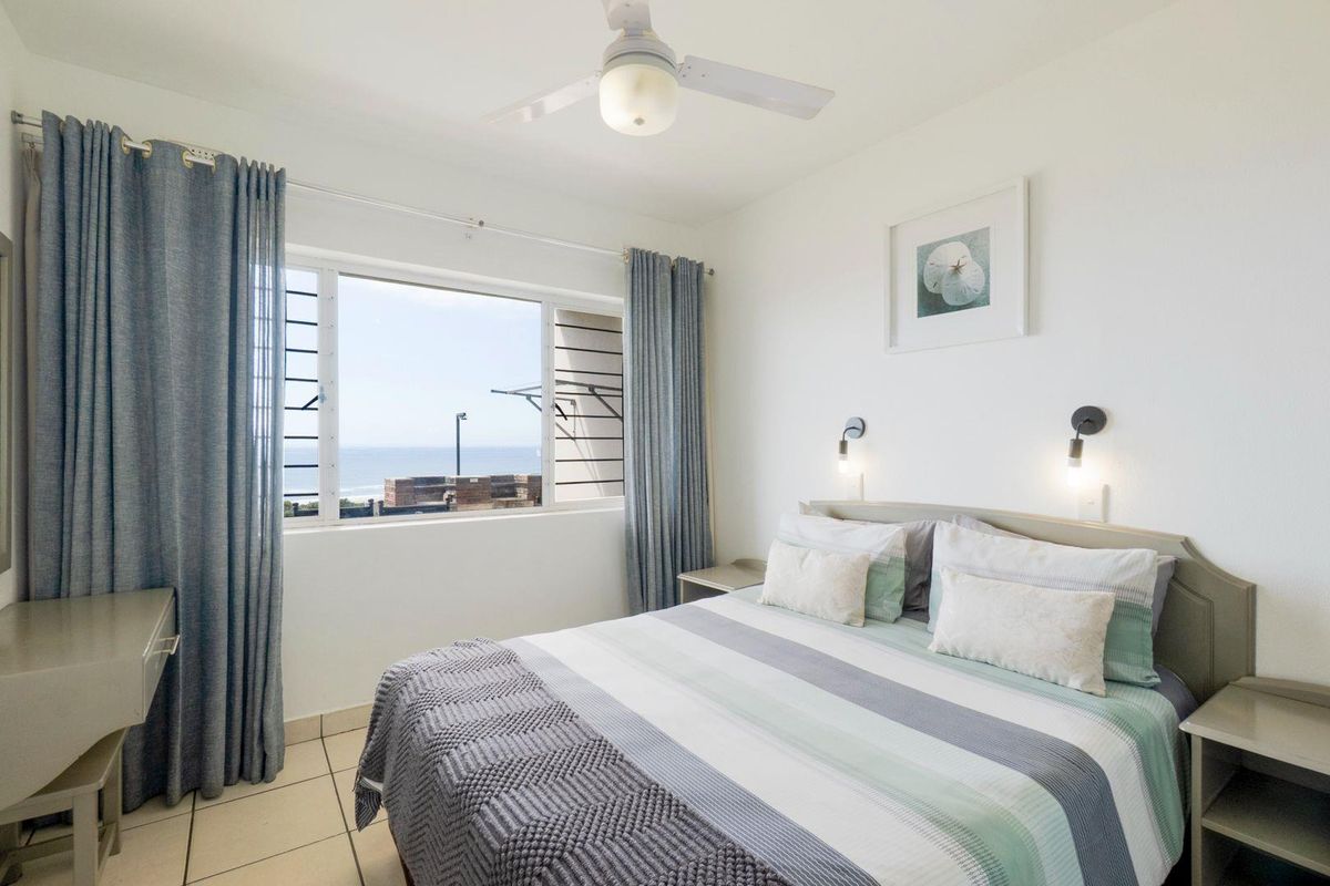 A bright bedroom featuring tiled flooring, a ceiling fan, and a window offering a view of the ocean.