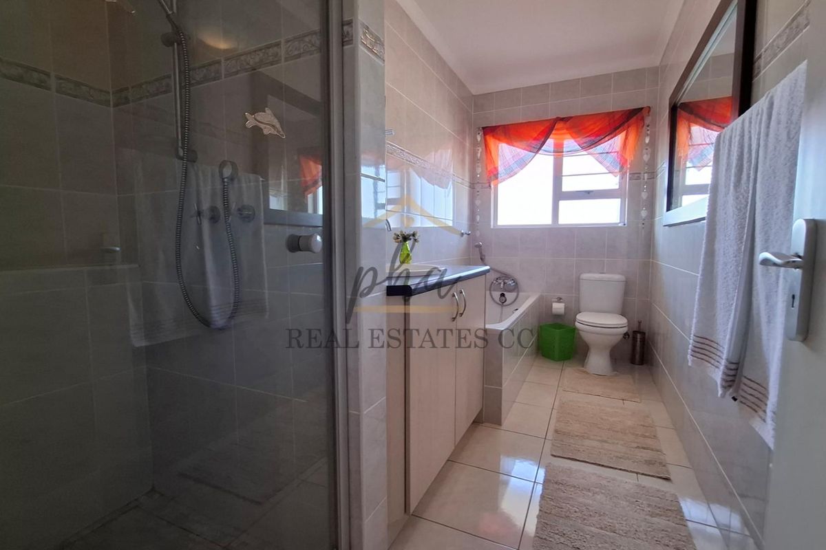 A functional bathroom featuring a glass-enclosed shower, a built-in vanity with countertop, a bathtub, and a toilet with neutral wall and floor tiling.