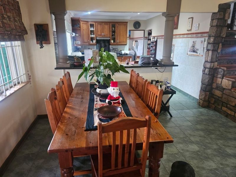 Open plan dining area featuring ceramic tile flooring, decorative columns, and a breakfast bar overlooking the kitchen with wooden cabinetry.