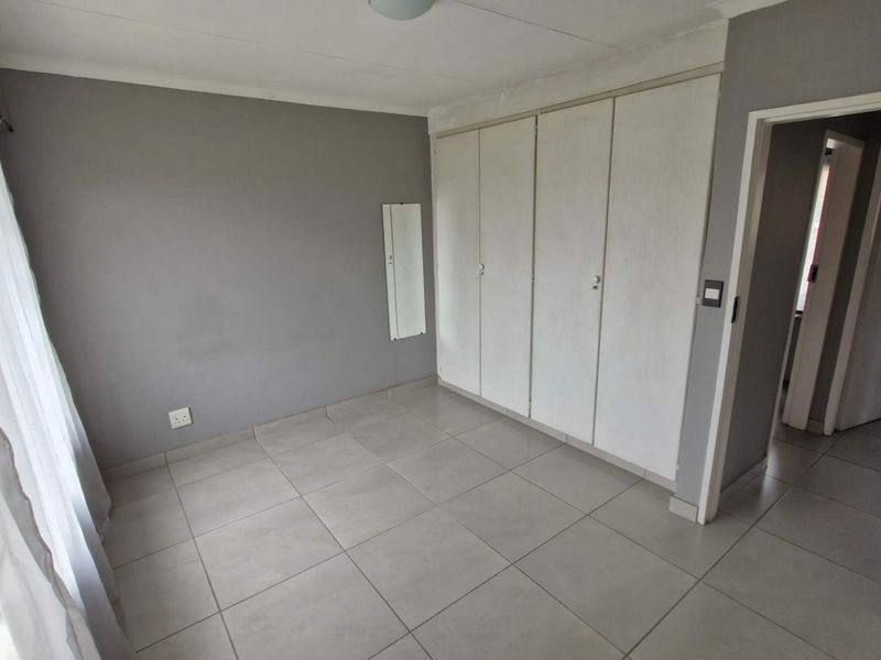 An empty bedroom featuring neutral grey walls, tiled flooring, and built-in storage cupboards.