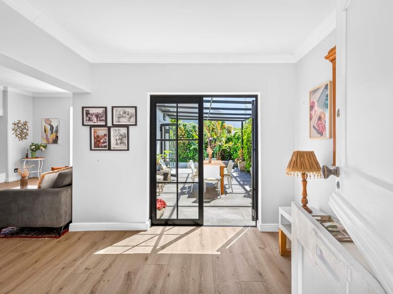 Bright living room featuring light wood-look laminate flooring, crown molding, and black-framed sliding doors providing seamless access to the outdoor patio area.