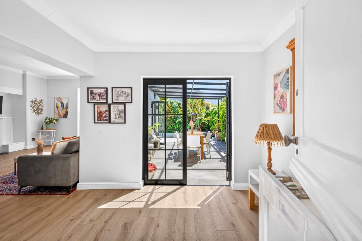 Bright living room featuring light wood-look laminate flooring, crown molding, and black-framed sliding doors providing seamless access to the outdoor patio area.