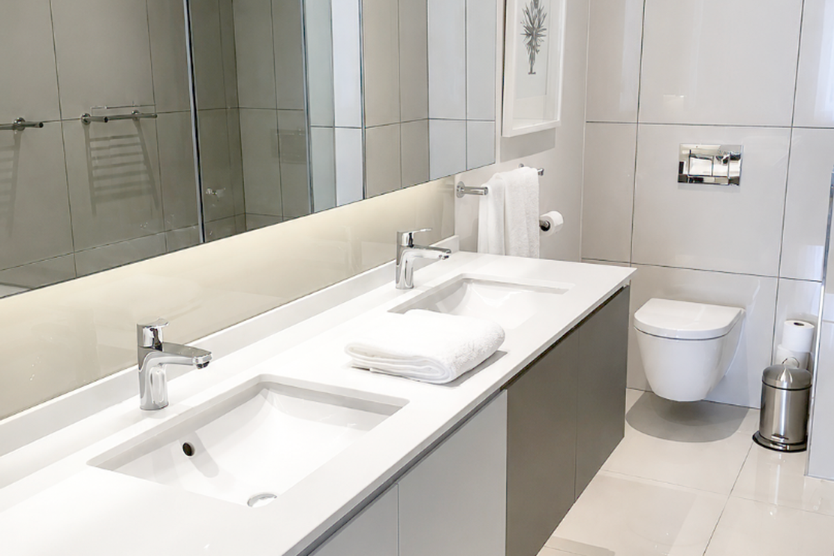 Modern bathroom featuring a sleek double vanity with integrated sinks, wall-mounted toilet, large mirror, and high-quality floor-to-ceiling tiling.