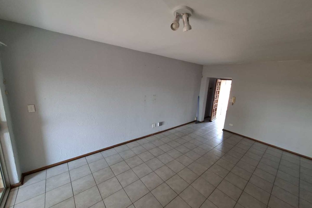 An empty, neutrally painted living area featuring tiled flooring and a ceiling-mounted light fixture, offering a blank canvas for interior design.