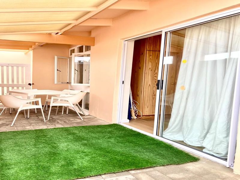 A covered patio area featuring paved flooring, artificial turf, and direct access to the interior through a large sliding glass door.