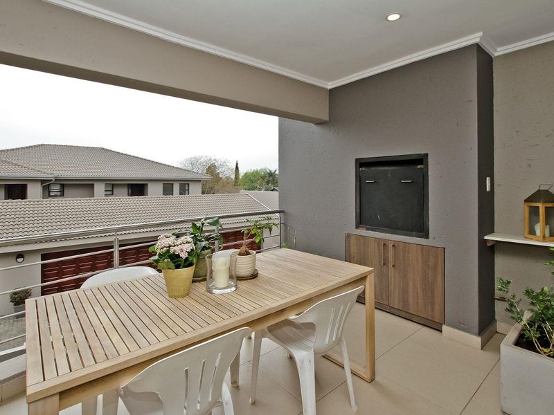 Covered balcony featuring a built-in braai, tiled flooring, and a metal balustrade, offering a functional outdoor entertainment space.