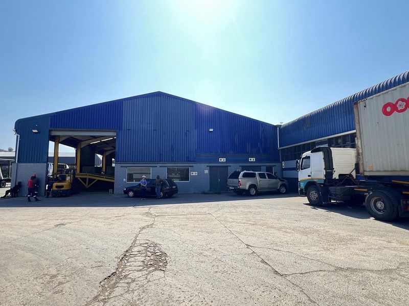 Industrial warehouse facility featuring a large blue metal-clad structure, expansive concrete yard, and multiple loading access points for heavy vehicles.