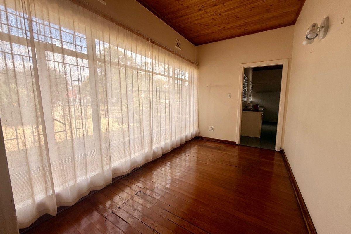 An empty living room featuring original timber flooring and a timber-paneled ceiling, offering a blank canvas for renovation.