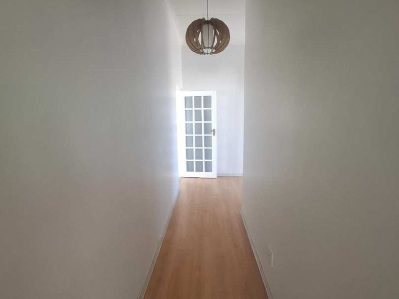 A bright, empty hallway featuring light wood-look laminate flooring and a classic white French door at the end.