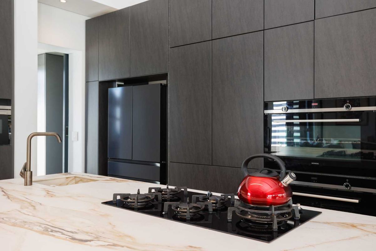Modern kitchen featuring dark cabinetry, a marble-look stone island countertop, integrated oven, and a built-in gas cooktop.