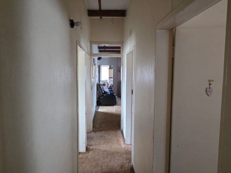 A narrow residential hallway featuring exposed ceiling beams and a transom window, currently showing signs of wear and requiring cosmetic updates.