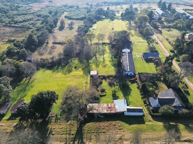 Aerial view of a rural farm property featuring multiple outbuildings, large open grazing fields, and established trees across the expansive landscape.