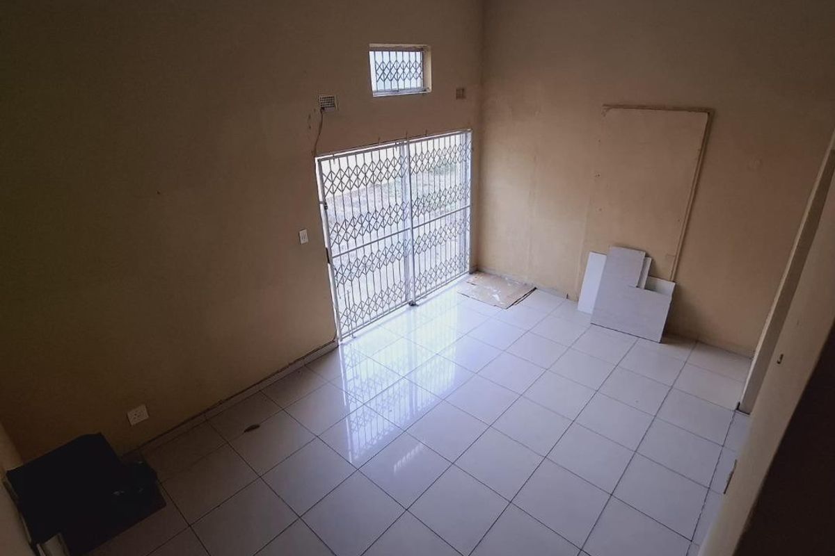 An empty living room featuring tiled flooring, a security gate, and security bars on the window, awaiting personal touches and cosmetic updates.