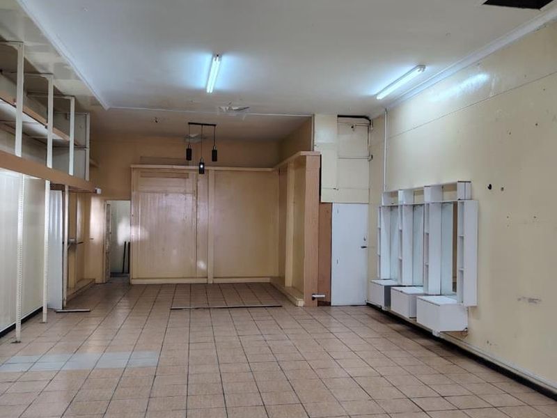 An empty commercial utility or retail space featuring tiled flooring, built-in shelving units, and fluorescent lighting, requiring cosmetic refurbishment.