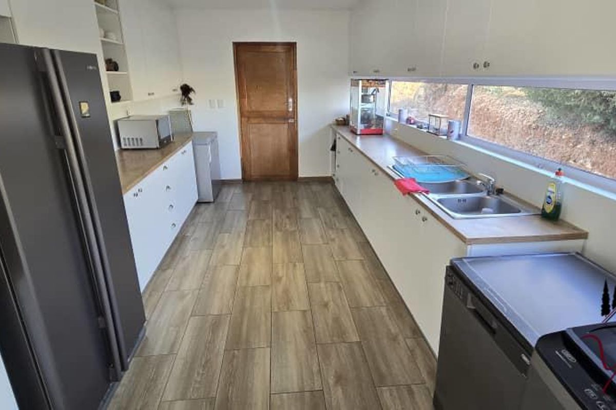 A functional galley-style kitchen featuring white cabinetry, wood-look countertops, a double stainless steel sink, and a long horizontal window providing natural light.