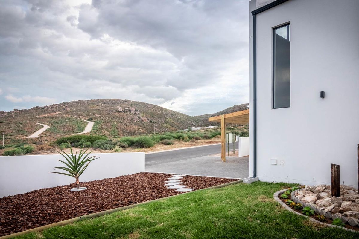 A modern exterior view featuring a landscaped garden with mulch, stone path, and a clean white facade against a scenic mountain backdrop.