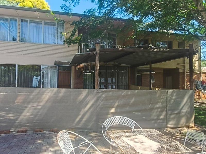 Rear view of a two-story house featuring a paved patio area, a covered outdoor structure, and an upper-level balcony.