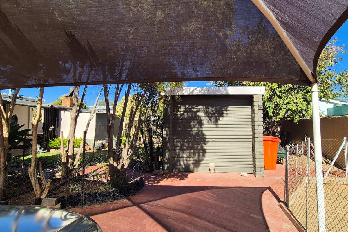Outdoor area featuring a paved driveway, a detached garage with a roller door, and a large shade sail structure providing cover.