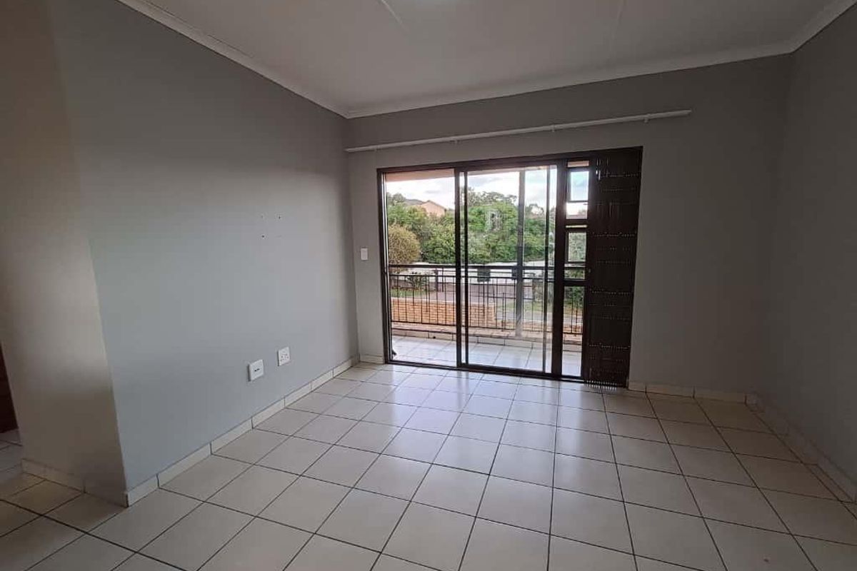 An empty living room featuring tiled flooring, neutral wall paint, and sliding glass doors that open onto a balcony.