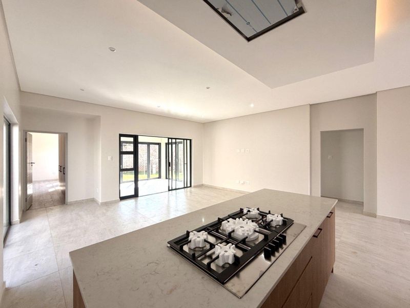 Spacious open-plan living area featuring a modern kitchen island with a gas hob, neutral tiled flooring, and large sliding doors leading to the patio.