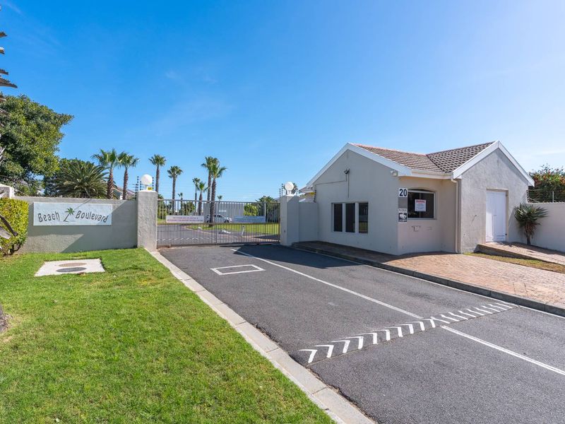 The entrance to Beach Boulevard complex featuring a secure gated access point, guard house, and well-maintained paved driveway.