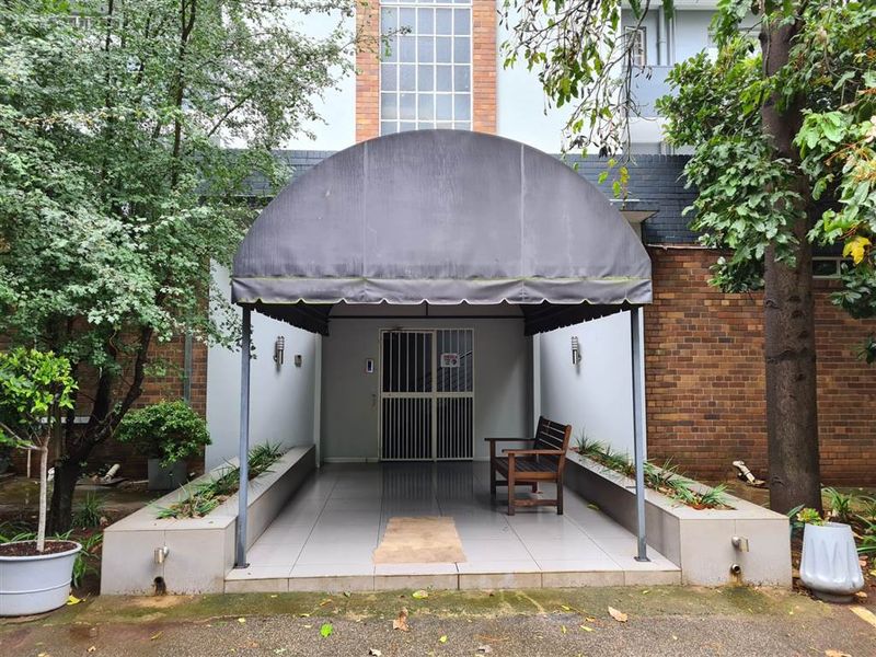 Front entrance of the apartment building featuring a covered porch with a fabric awning, security gate, and brick facade detailing.