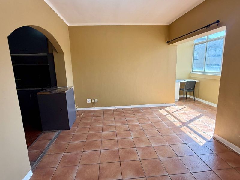 An open-plan living area featuring tiled flooring, an arched entryway, and a large window providing natural light.