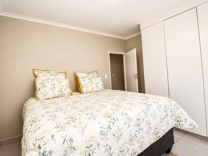 A well-maintained bedroom featuring neutral wall tones, tiled flooring, and ample built-in cupboard storage.