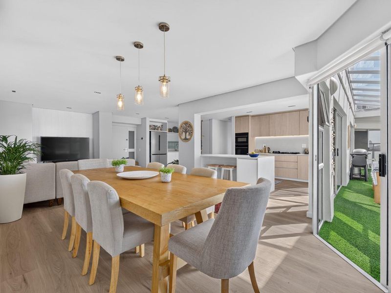 Modern open-plan living and dining area featuring a sleek kitchen with integrated appliances, light wood cabinetry, and seamless access to an outdoor patio space.