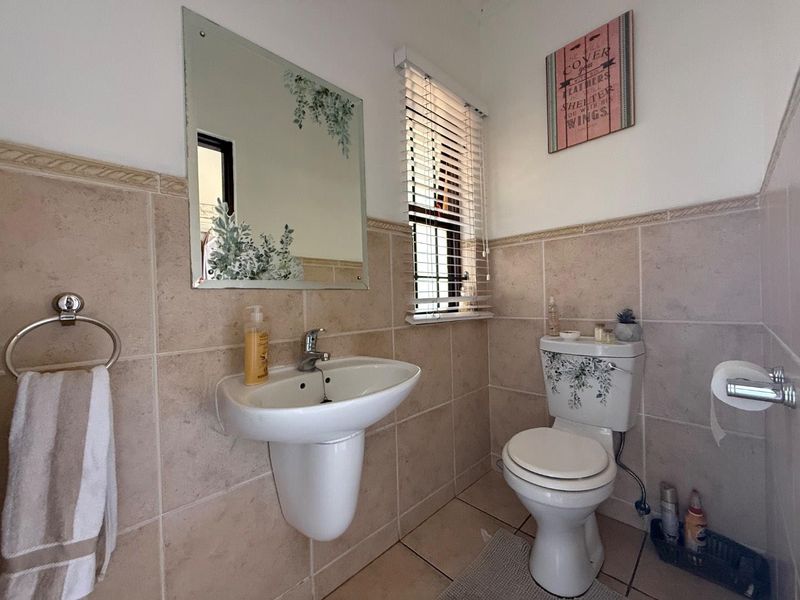 A compact guest bathroom featuring a pedestal basin, toilet, and neutral wall tiling with a window for natural light.