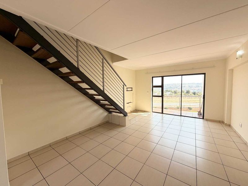 Spacious open-plan living area featuring tiled flooring, a modern staircase with metal balustrade, and large sliding glass doors leading to a balcony with views.