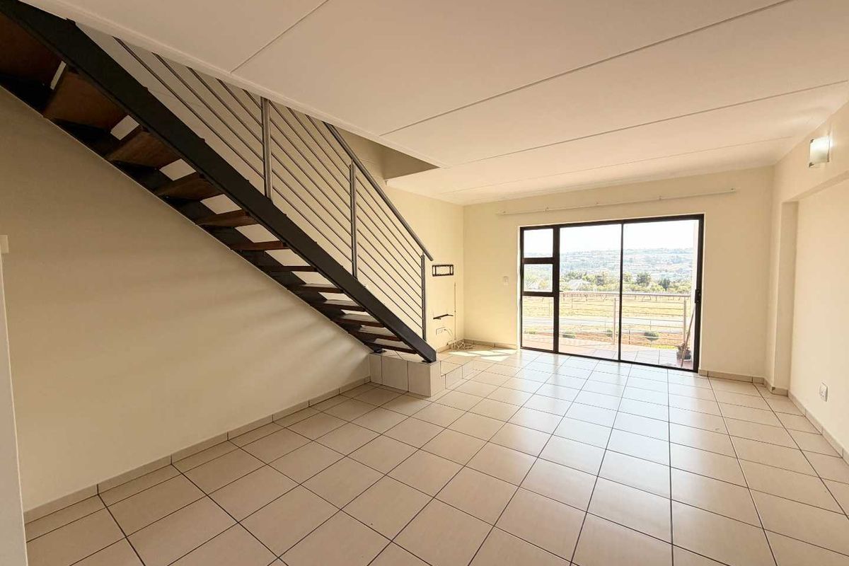 Spacious open-plan living area featuring tiled flooring, a modern staircase with metal balustrade, and large sliding glass doors leading to a balcony with views.