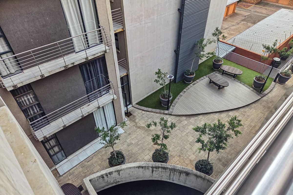 An elevated view of the apartment complex courtyard featuring paved walkways, landscaped garden beds, and a modern composite deck area.