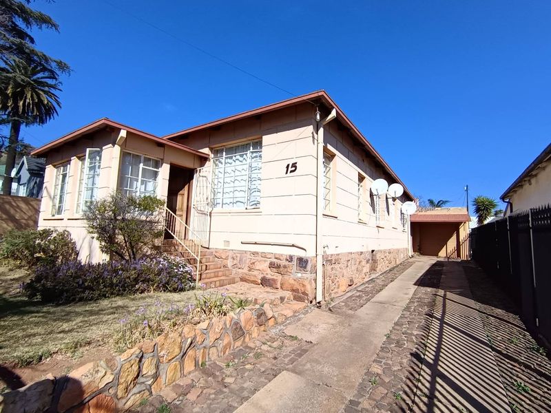 Front elevation of a single-story house featuring stone cladding, a concrete driveway, and an attached carport.