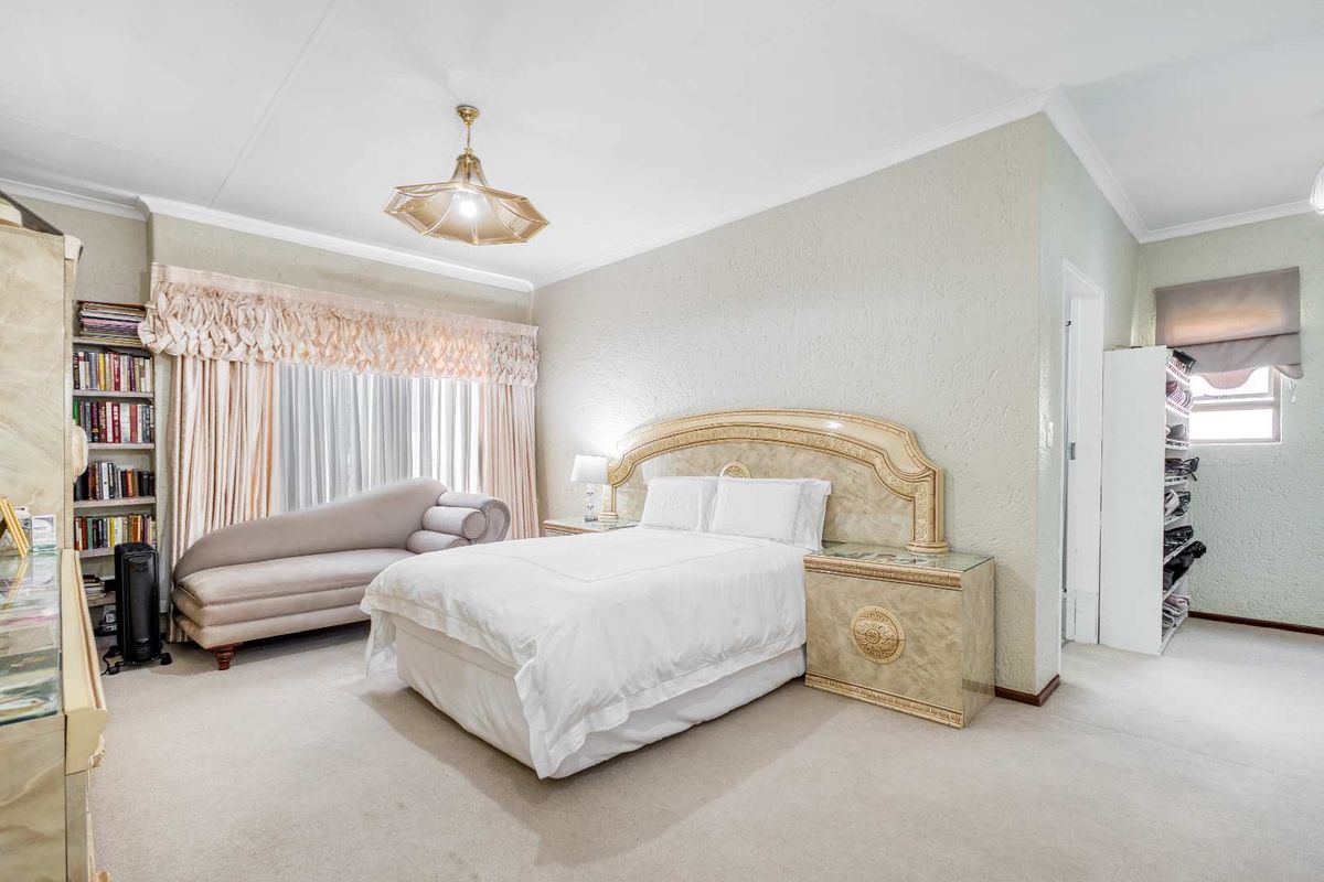 A spacious bedroom featuring textured walls, neutral carpeting, and classic ceiling cornicing, offering a comfortable and well-maintained living space.